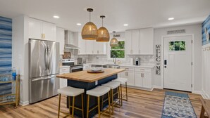 Una cocina moderna con armarios blancos, un refrigerador de acero inoxidable, una isla de madera con taburetes de bar y una alfombra azul estampada.