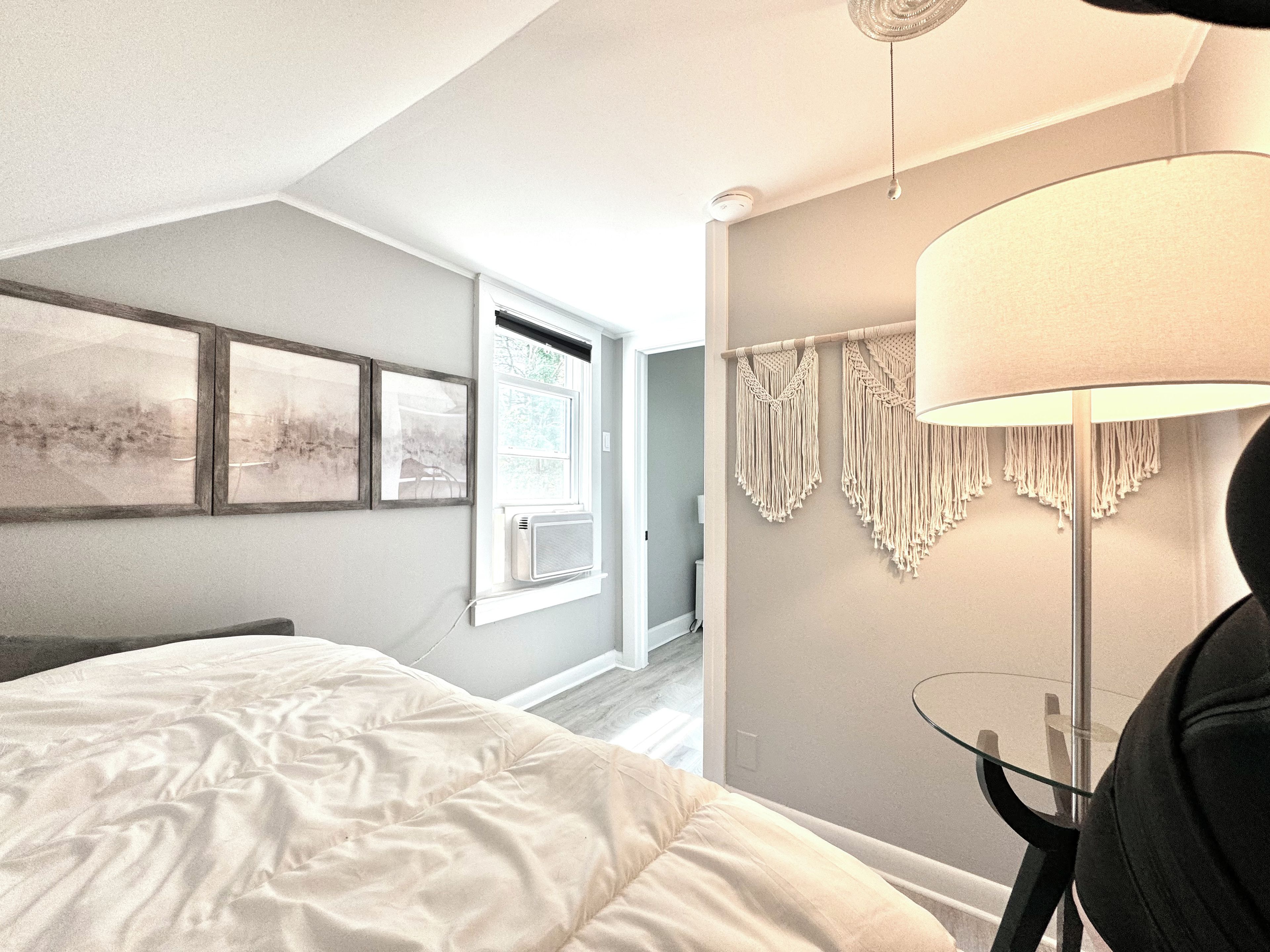 Ein Schlafzimmer mit einem Bett, einem Fenster, einer Wandklimaanlage und einem Wandbehang aus Makramee.