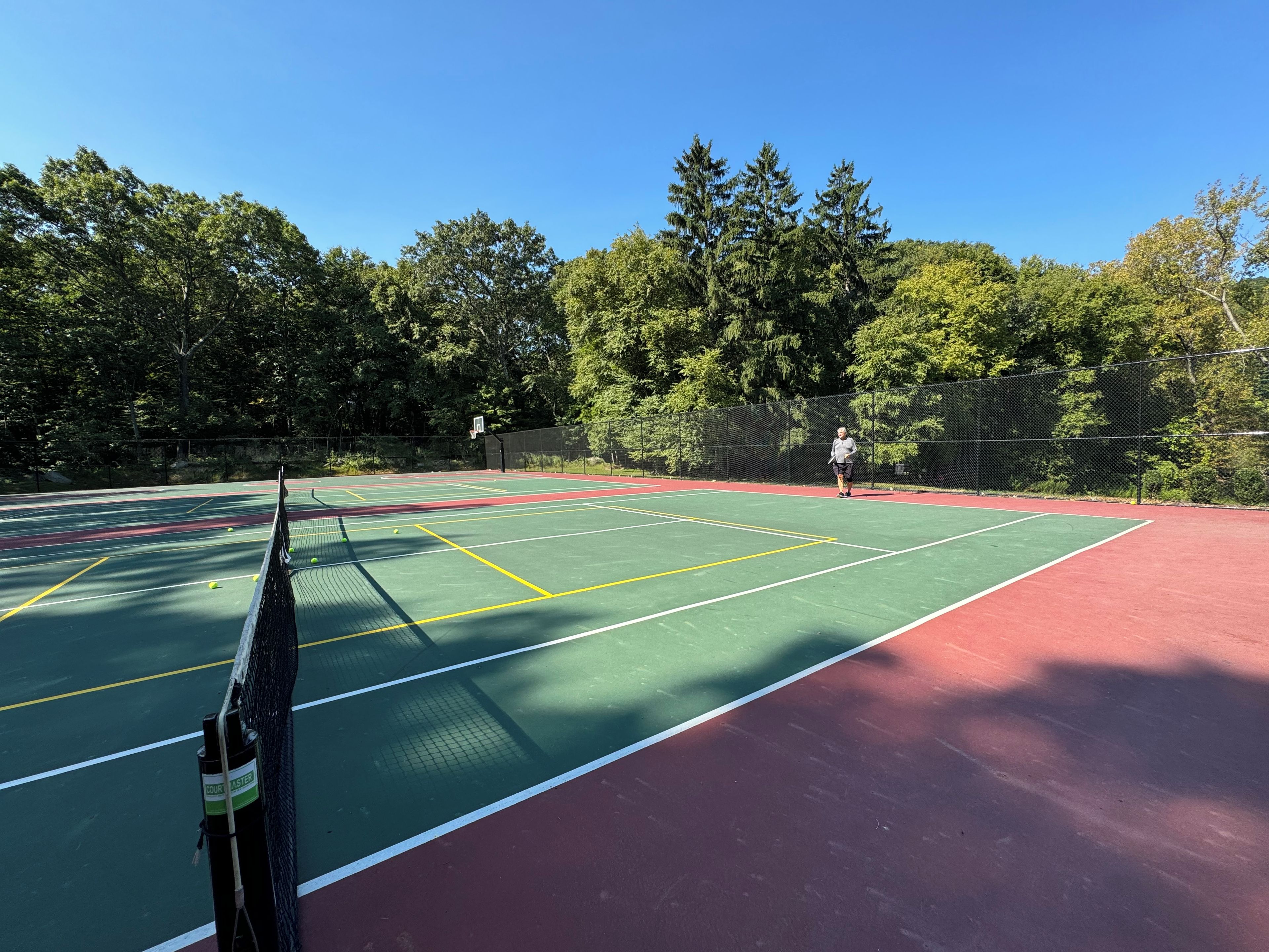 Ein Tennisplatz mit Netz, umgeben von Bäumen und einem Zaun.