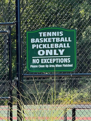 Een bordje op een hek dat aangeeft dat dit gebied uitsluitend bestemd is voor tennis, basketbal en pickleball, met de herinnering om na gebruik op te ruimen.