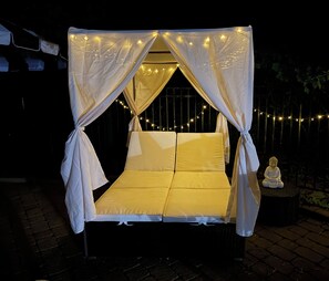 Een bed met hemelbed en verlichting, omringd door een hek en een Boeddhabeeld.