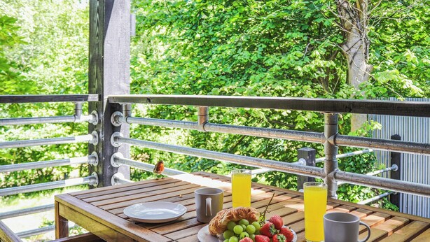 Une table en bois sur laquelle sont disposés des aliments pour le petit-déjeuner, notamment des raisins, des fraises, un croissant et deux verres de jus d’orange.