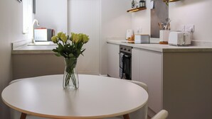 Une cuisine moderne avec des meubles blancs, une table de salle à manger ronde et un vase rempli de roses jaunes.