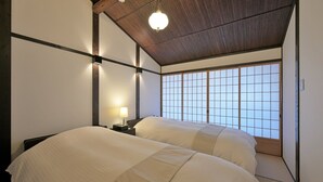 A traditional Japanese-style room with tatami flooring, two beds with white bedding, a shoji screen window, and a wooden ceiling. - Takeya Tenmangu (Kyoto)