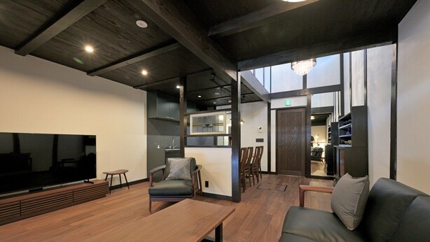 A modern living room with a large flat-screen TV, wooden flooring, a sofa, a coffee table, and a dining area with chairs. - Takeya Tenmangu (Kyoto)