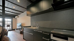 A modern kitchen with dark cabinetry, a stainless steel sink, and a patterned backsplash. - Takeya Tenmangu (Kyoto)