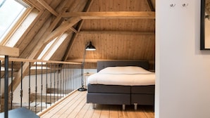 Una camera da letto con soffitto spiovente, un letto, un comodino, una lampada e una finestra.