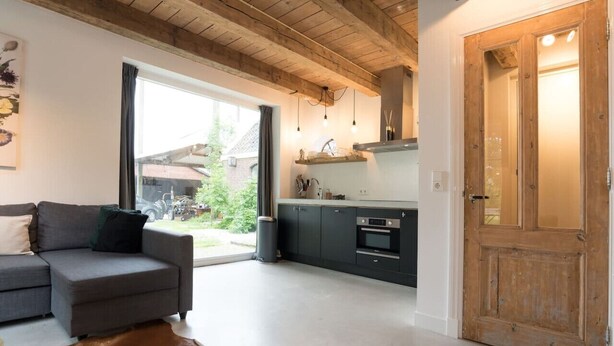 Una cucina moderna con mobili scuri e soffitto in legno, un divano grigio con tappeto marrone e un'ampia porta in legno.