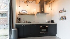 Una cucina moderna con mobili scuri, forno integrato e una finestra vista un muro di mattoni e una bicicletta all'esterno.