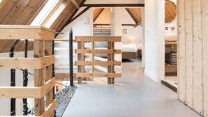 Un pasillo estrecho con vigas de madera y techo inclinado, que conduce a un dormitorio con cama y mesita de noche.