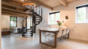 Un amplio espacio habitable con una escalera de madera, una mesa de comedor con sillas y un sofá.