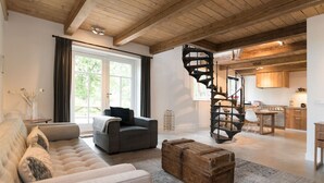 Un espacio de sala amplio con un sofá grande, un cofre de madera y una escalera espiral que lleva a una cocina.