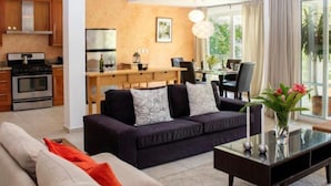 A modern living room with a sofa, coffee table, and a dining area with a table and chairs.