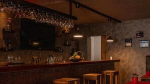 A bar area with wooden stools, a counter with glassware, and a television mounted on the wall.