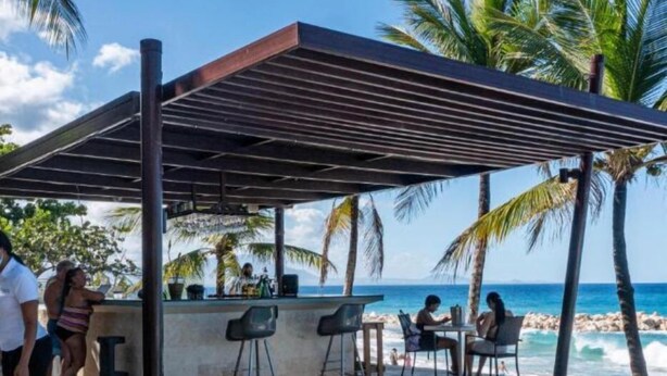 A poolside area with a covered seating area, a bar, and a view of the ocean.
