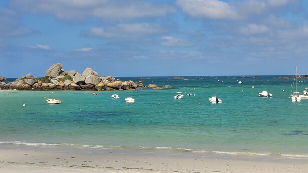 A beach with clear turquoise waters, large rocks, and several boats.