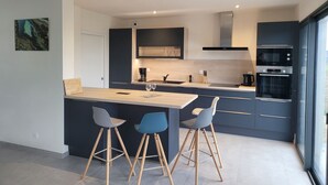 A modern kitchen with a central island, bar stools, and a large window.