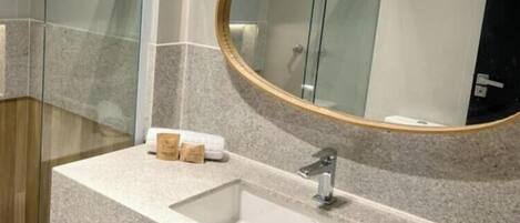A bathroom with a granite countertop, a sink, a mirror, and a glass shower enclosure.