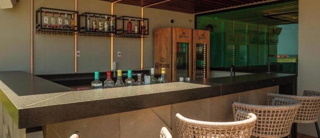 A bar area with a counter, bottles, and wicker chairs.
