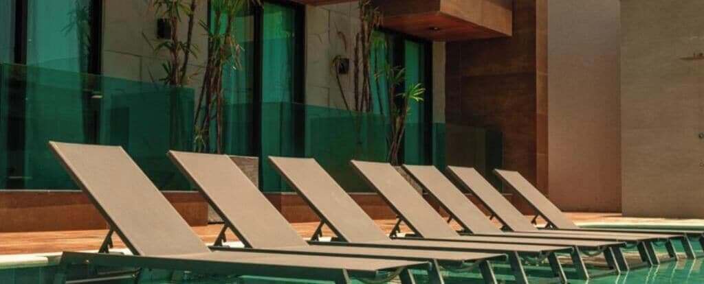 A pool area with lounge chairs and a glass wall.