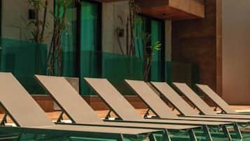 A pool area with lounge chairs and a glass wall.