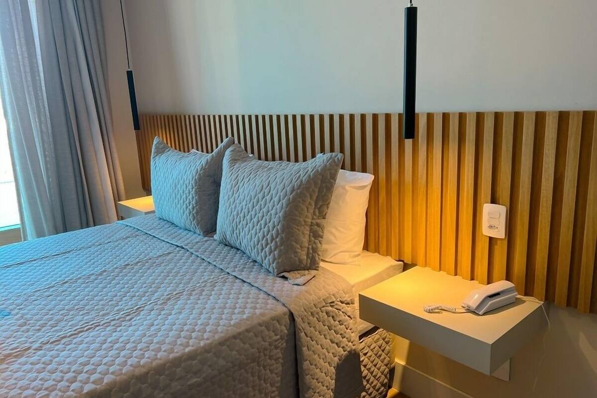 Camera d'albergo con un letto, due cuscini, un comodino con il telefono e una parete con listelli di legno verticali.