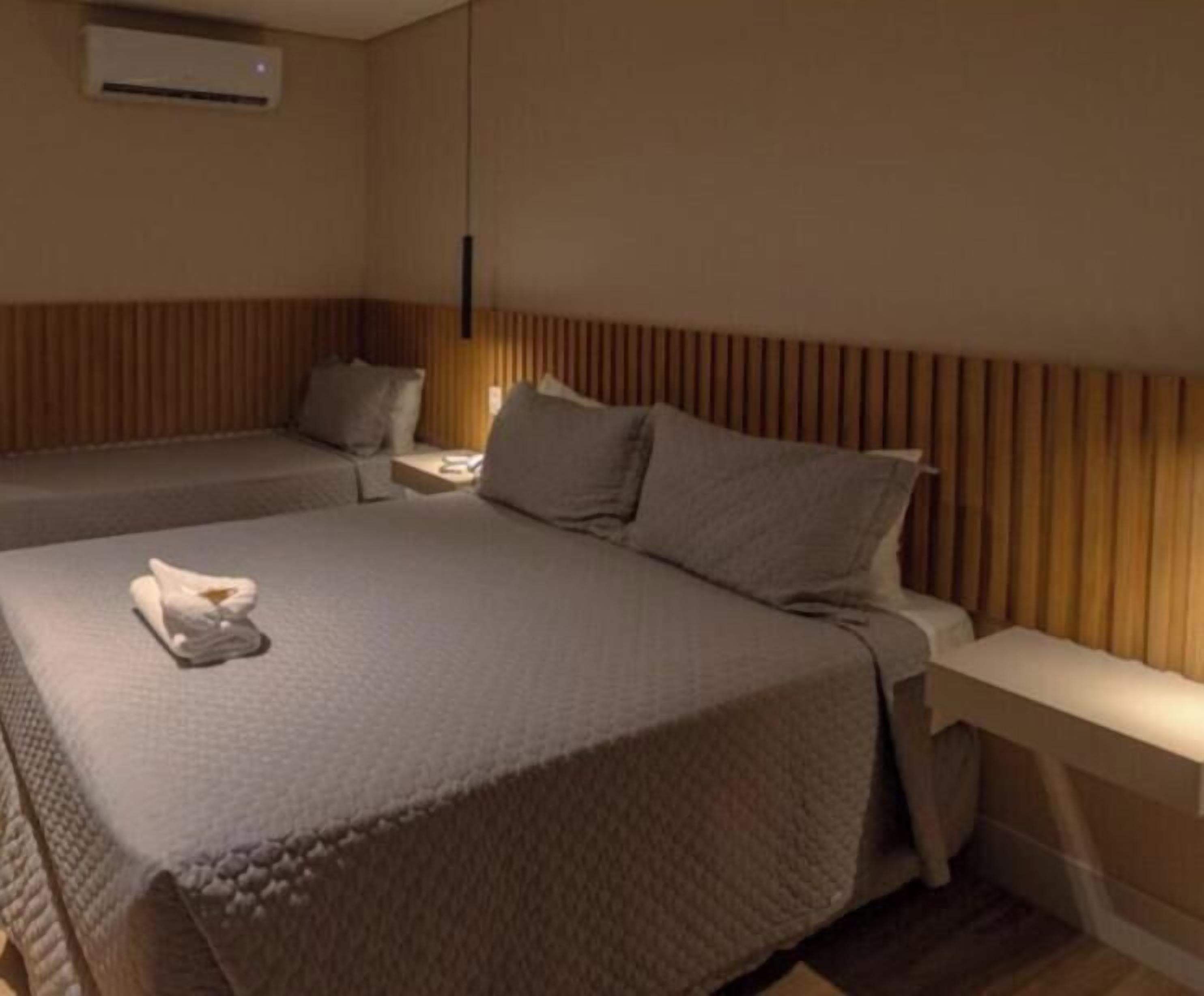 A hotel room with two beds, a bedside table, a lamp, and an air conditioning unit.