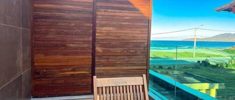 A balcony with a wooden chair and table, overlooking a coastal landscape with a clear sky.