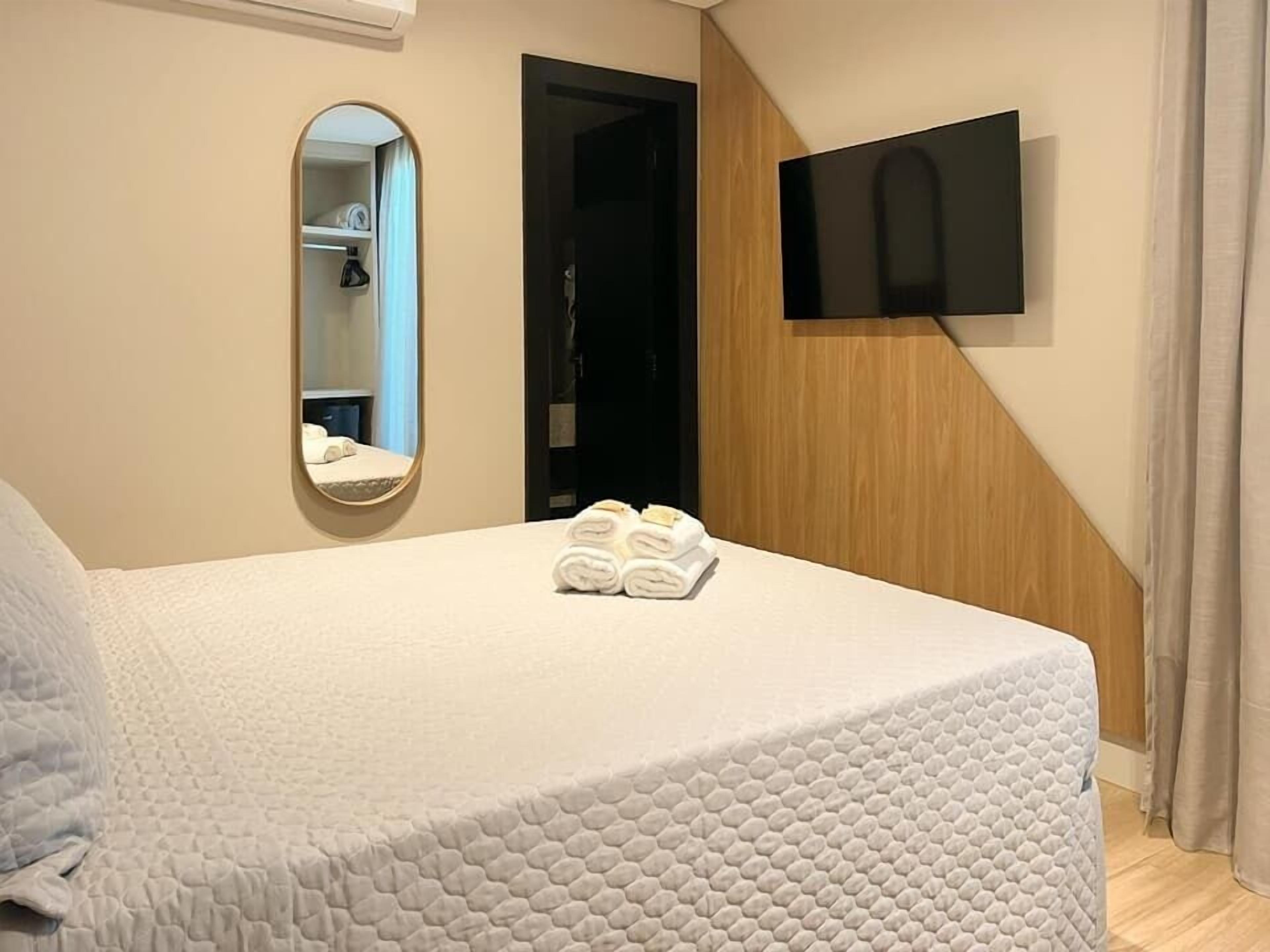 Una habitación de hotel con una cama, un televisor de pantalla plana en la pared y un espejo.