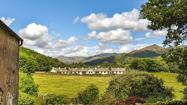 A stone wall, a grassy field, and a row of houses with a mountain in the background.