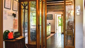 A hallway with wooden beams, a reception desk, and a glass door with a view of greenery outside.