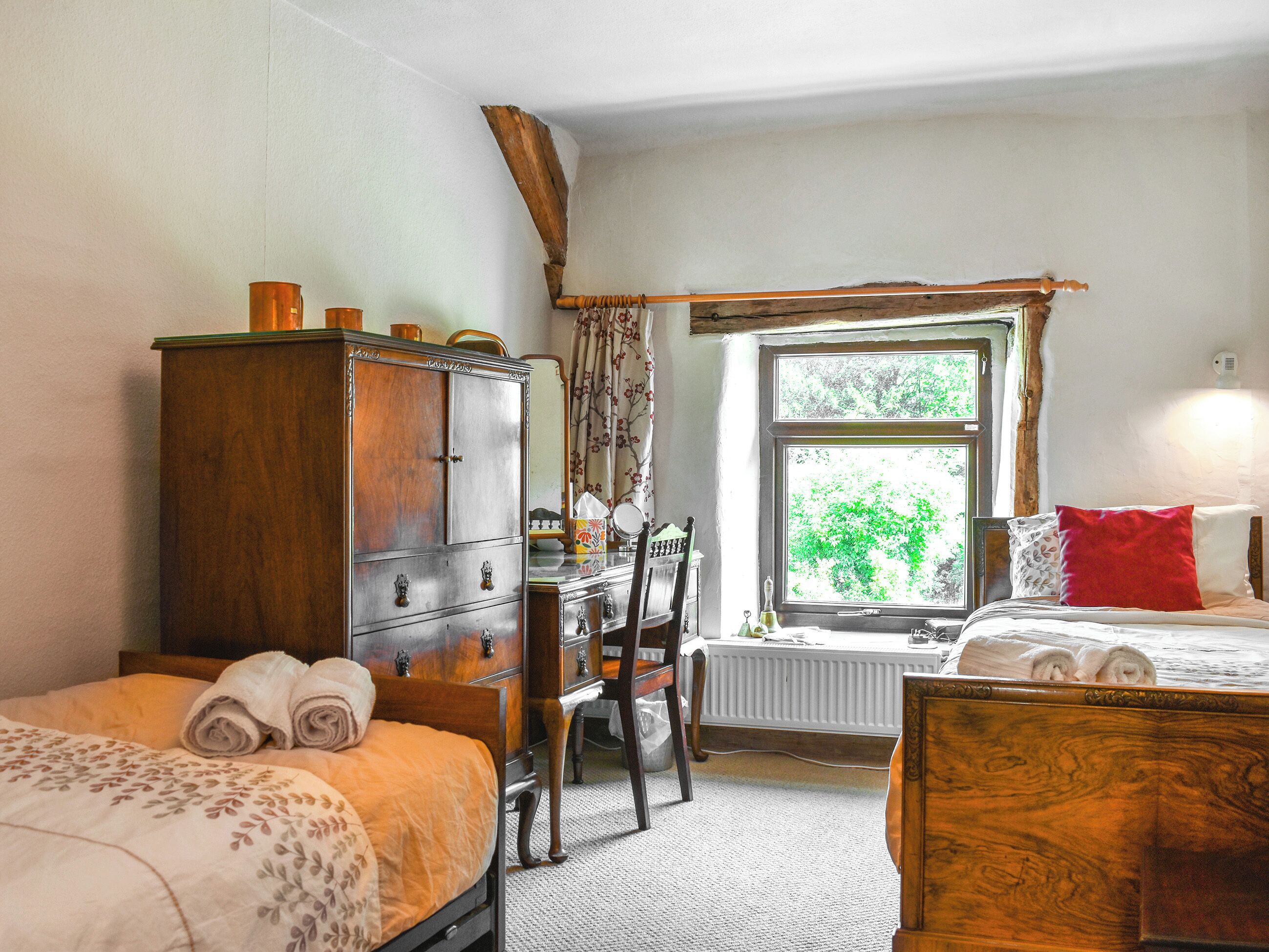 A bedroom with two beds, a wooden dresser, a chair, and a window with a view of trees.