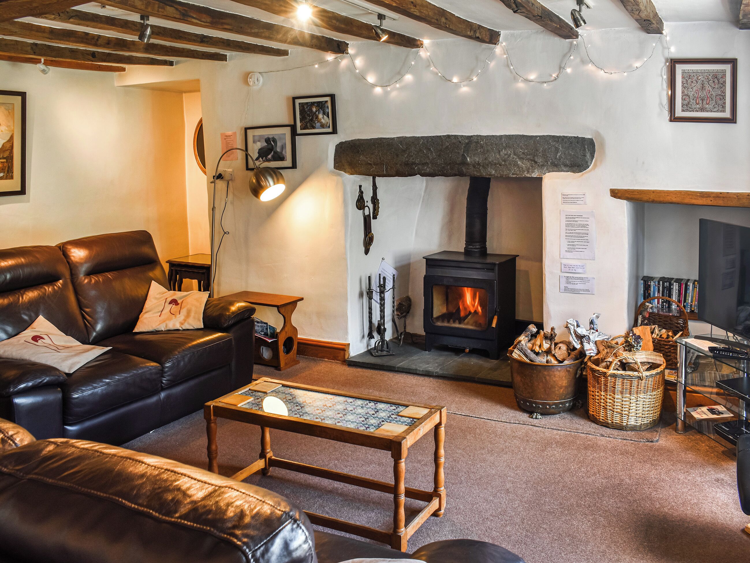 A cozy living room with a fireplace, leather sofa, wooden coffee table, and string lights.