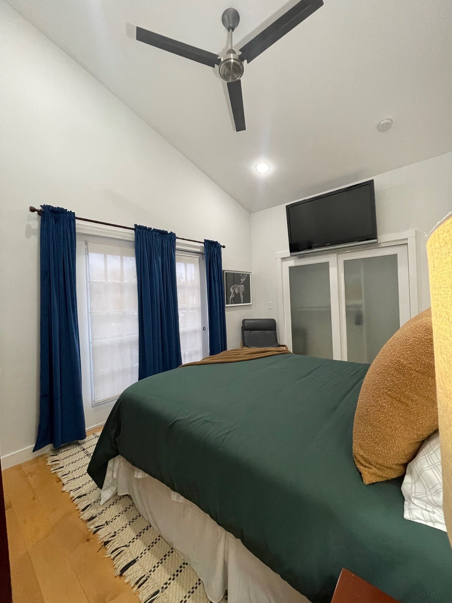 Quarto com cama, ventilador de teto, televisão na parede e janela com cortinas.
