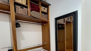 Un dressing accessible sans porte, doté d’étagères en bois, de paniers et de barres pour suspendre les vêtements.
