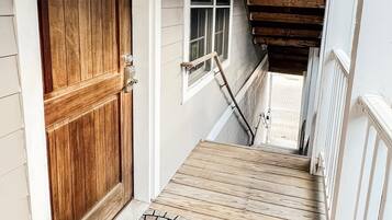 Eine Holztür, ein Fenster und eine Treppe mit einem Holzgeländer. Darunter liegt eine gemusterte Fußmatte.
