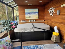 Quarto moderno com uma janela grande, um quadro de uma cena de praia, parede de madeira, cama, mesa pequena e um vaso com planta.