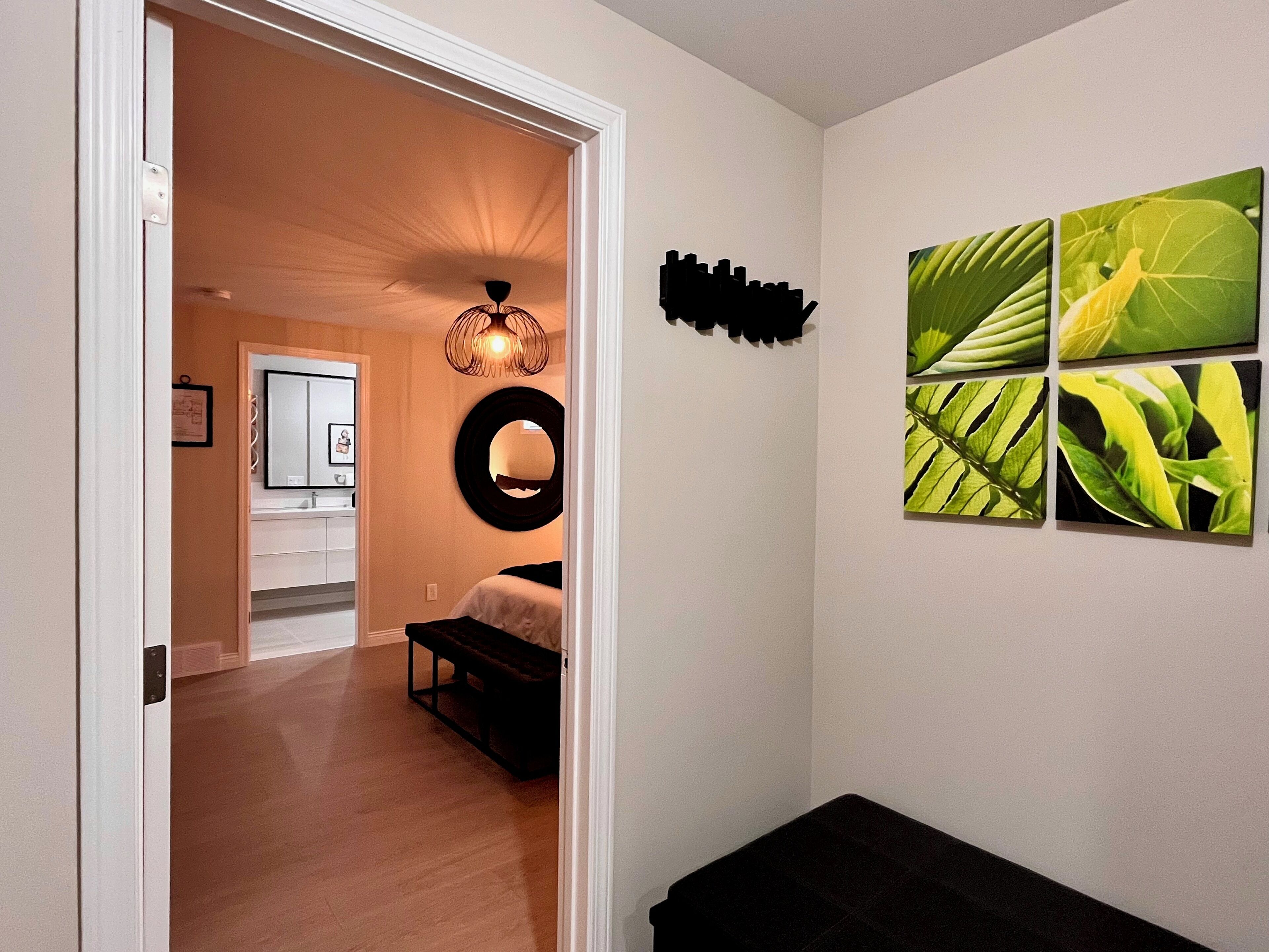 Un couloir avec un plancher en bois, un lit, un miroir et un luminaire fixé au mur.