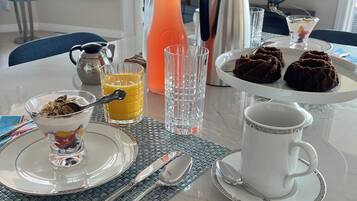 Una mesa de desayuno con una cafetera, un jarro, un vaso de jugo de naranja, un vaso de agua, un plato de galletas, una taza de café y un bol de parfait de yogur.