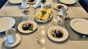 Une table en marbre dressée pour le petit-déjeuner, avec des assiettes remplies de nourriture, des tasses et un pichet de jus.