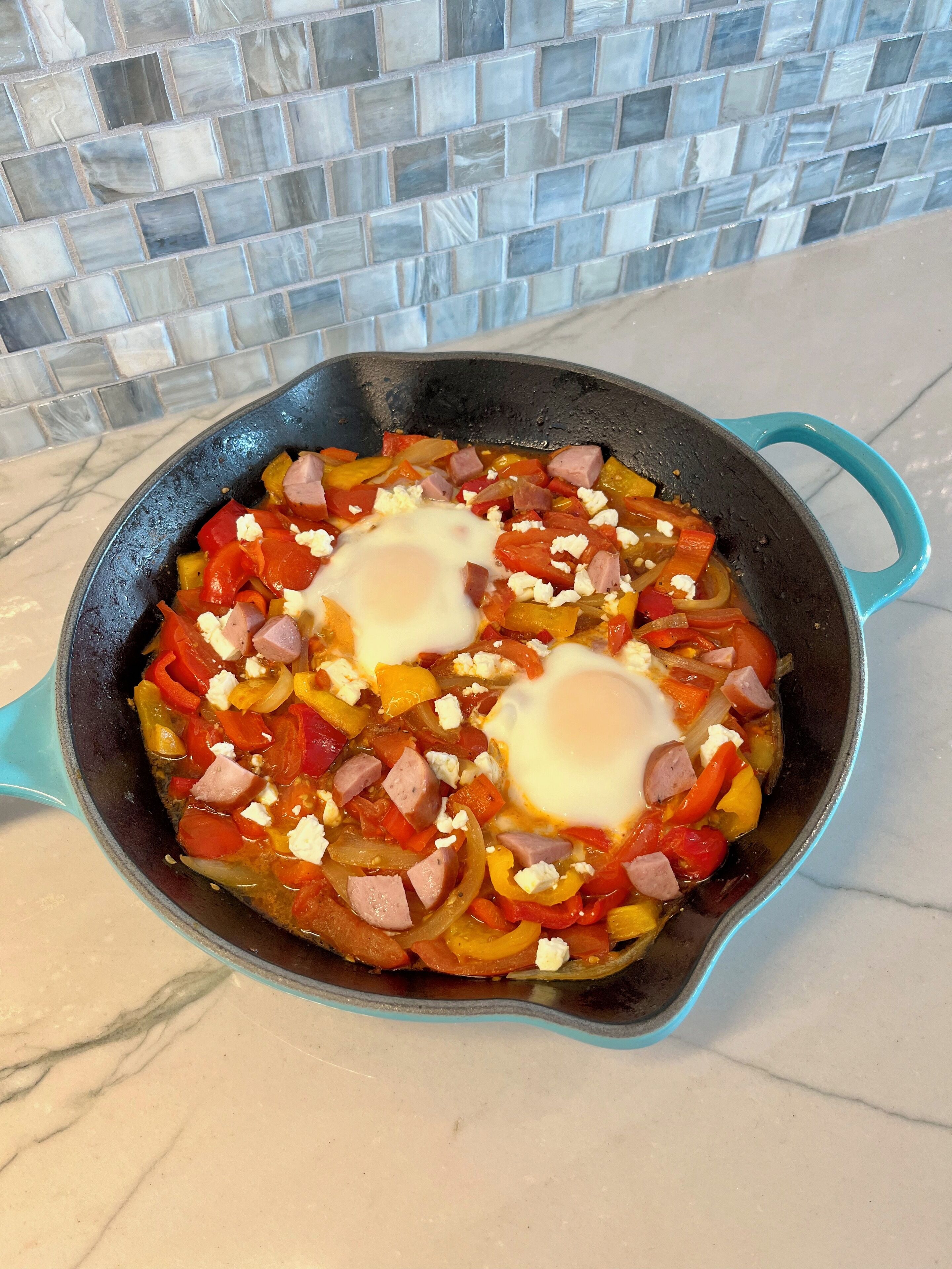 Una sartén con un plato que lleva huevos, salchicha y verduras.