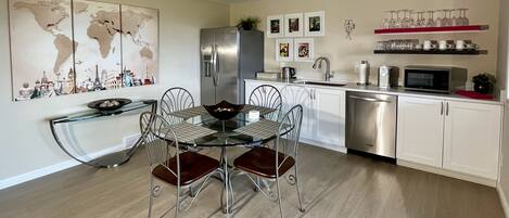 A modern kitchen with white cabinets, stainless steel appliances, and a glass dining table with metal chairs.