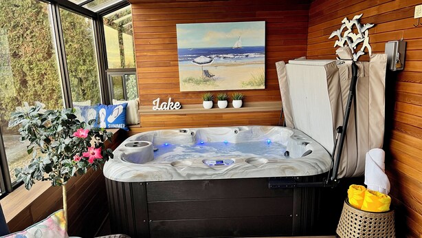 Une pièce avec un jacuzzi, des murs en bois, un tableau représentant une plage et une vue sur les arbres.
