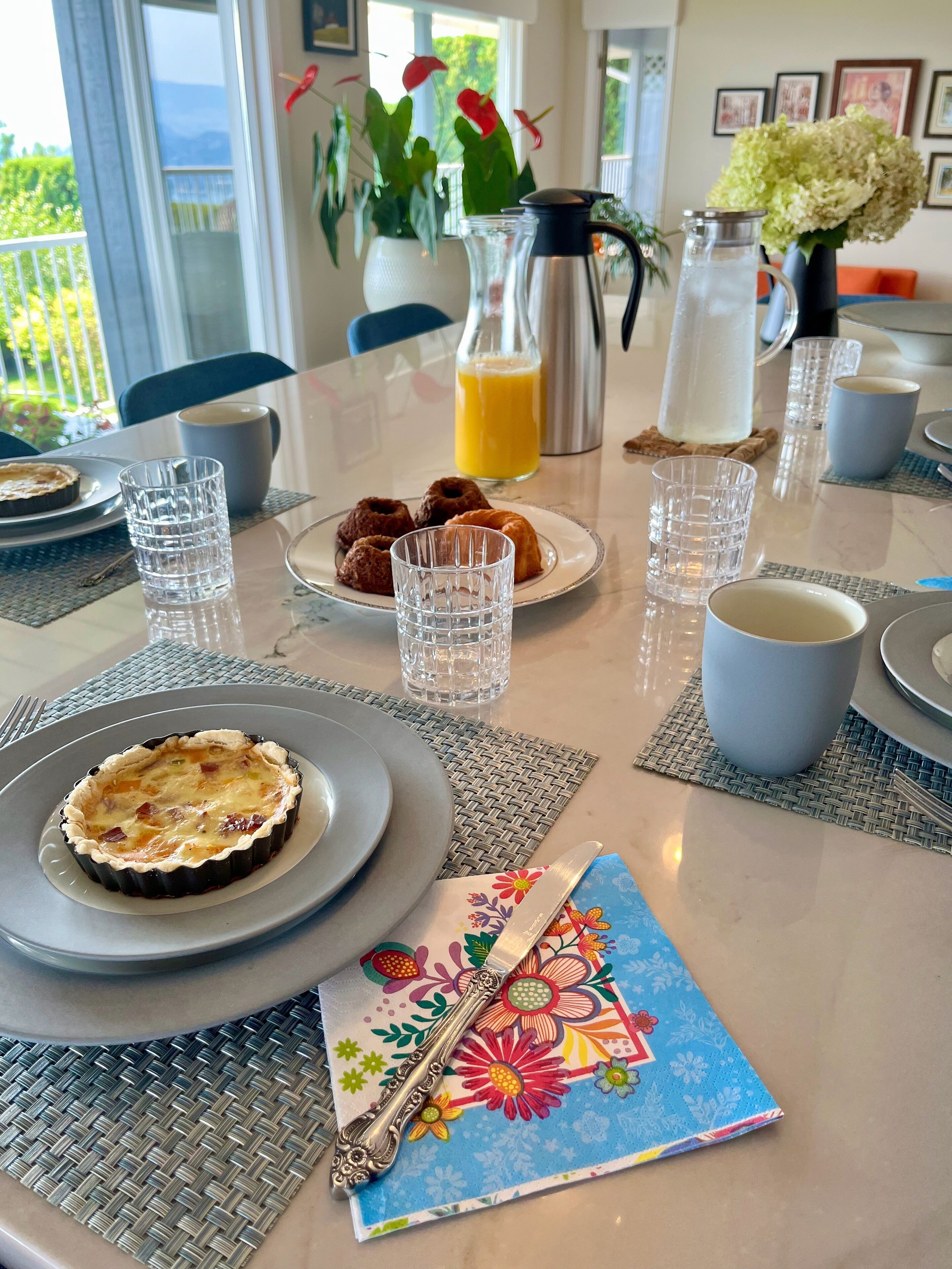Een ontbijttafel gedekt met borden, glazen, een koffiepot, een karaf en een decoratieve servet.