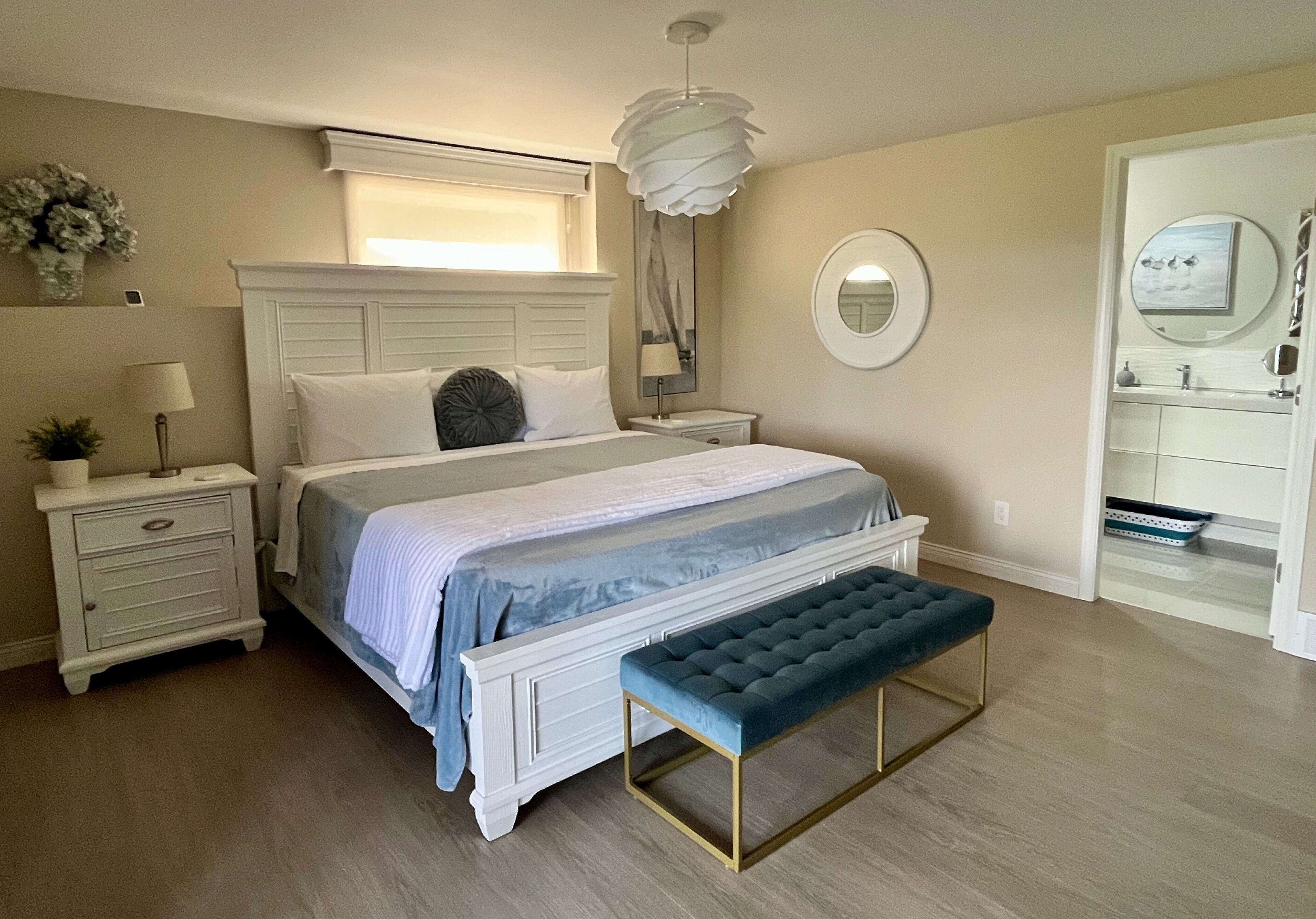 A bedroom with a bed, bedside tables, a bench, a mirror, and a window.