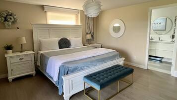 A bedroom with a bed, bedside tables, a bench, a mirror, and a window.
