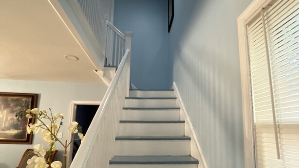 Una escalera con barandillas blancas y escalones azules, que conduce a una plataforma con un cuadro enmarco y un jarrón de flores.