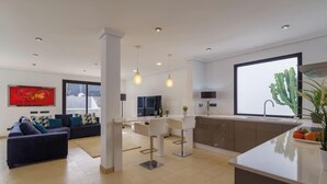 Una sala moderna con un sofá, un comedor con sillas, una cocina con mostrador y un ventanal grande.