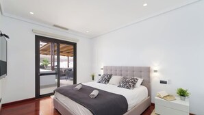 Un dormitorio moderno con una cama grande, una puerta corrediza de vidrio a un balcón, una mesita de noche con lámpara y una pequeña planta en maceta.