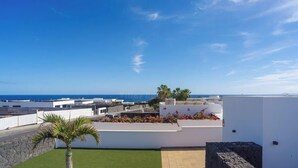 Una azotea con vistas al mar, una palmera y un edificio blanco con un parterre de flores.